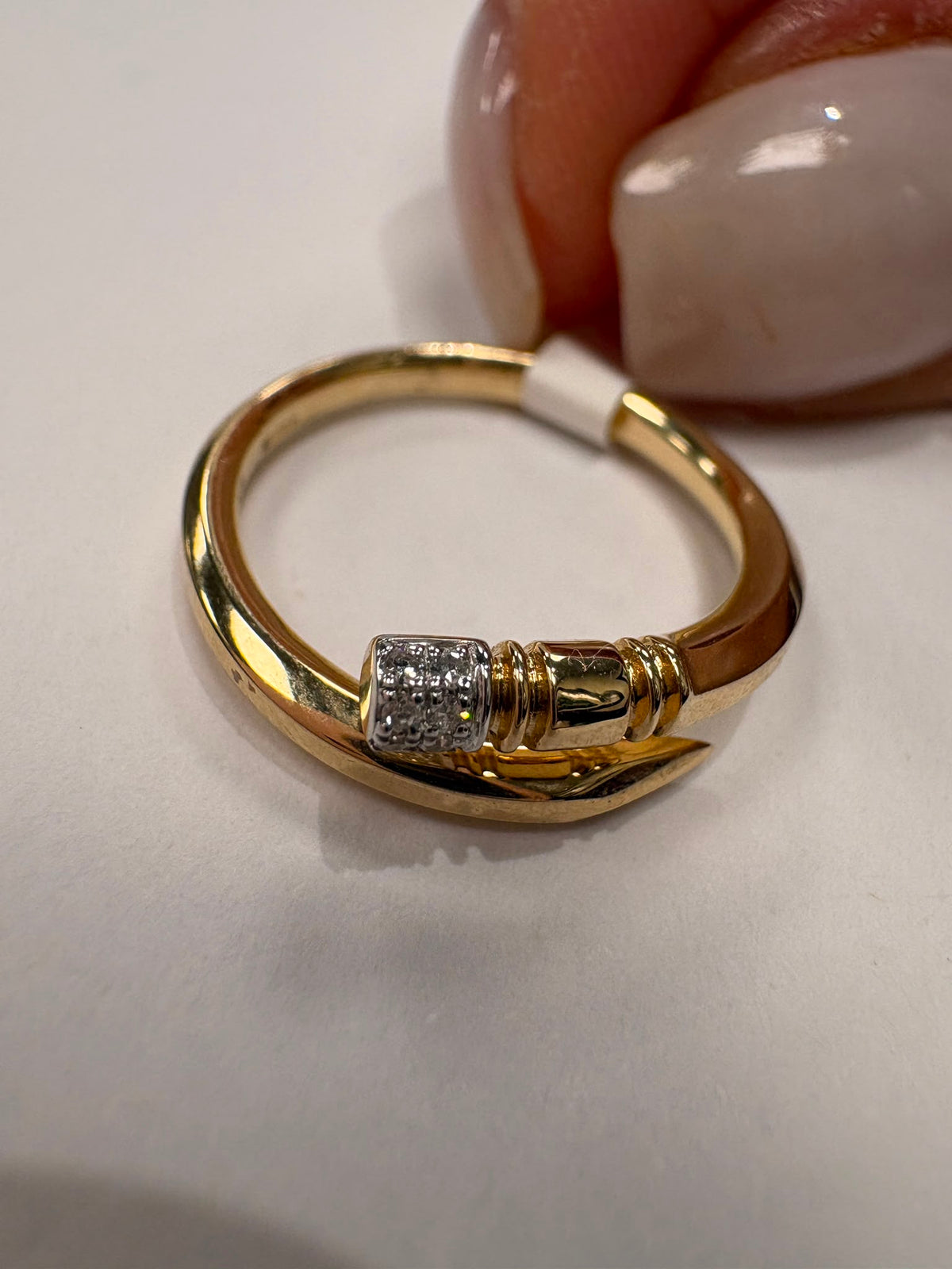 A gold ring with a textured, diamond-like silver band in the center, held by a hand with manicured nails against a plain white background.