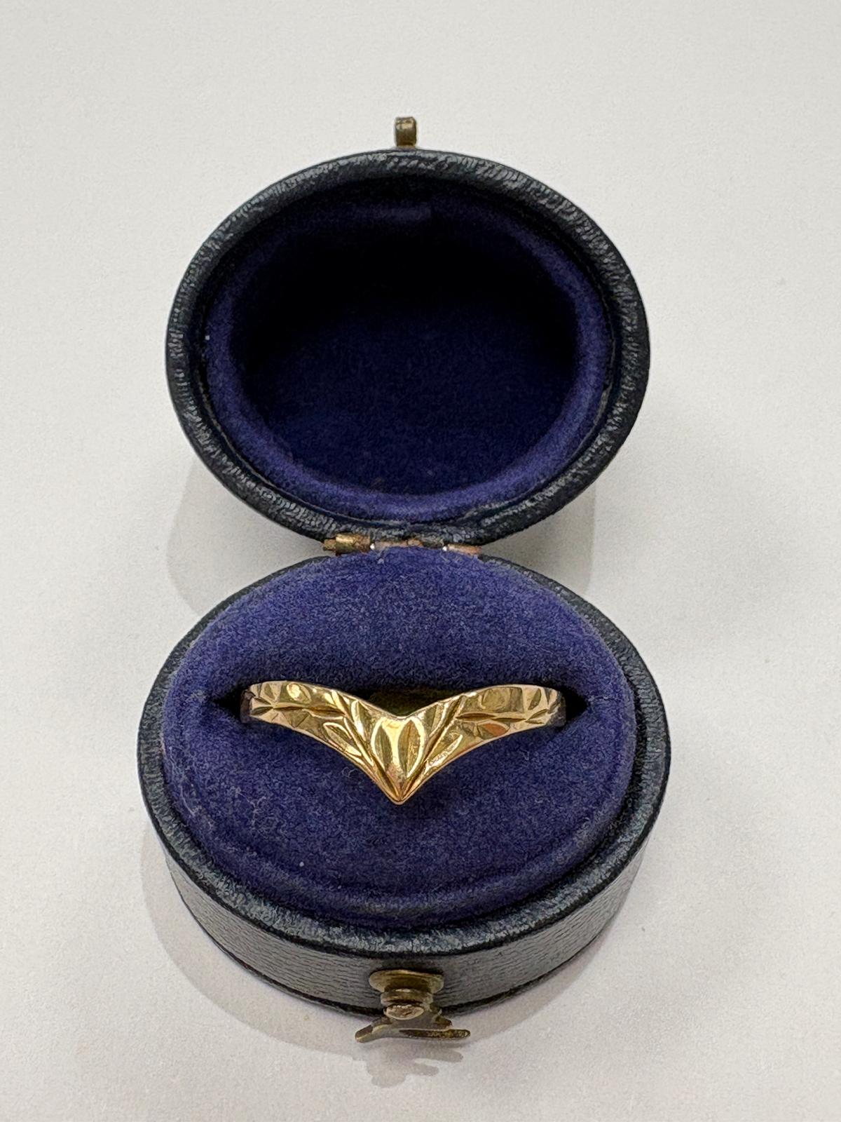 A gold ring with a textured, leaf-like or wing-like engraved pattern, displayed inside an open round presentation box with a dark blue velvet interior.