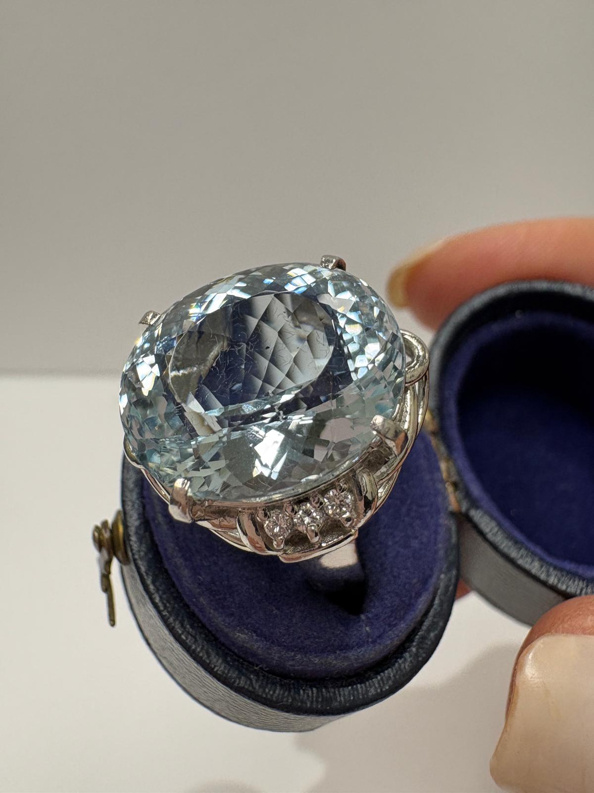 A large oval-cut aquamarine ring in a silver-toned setting, displayed on top of a vintage ring box