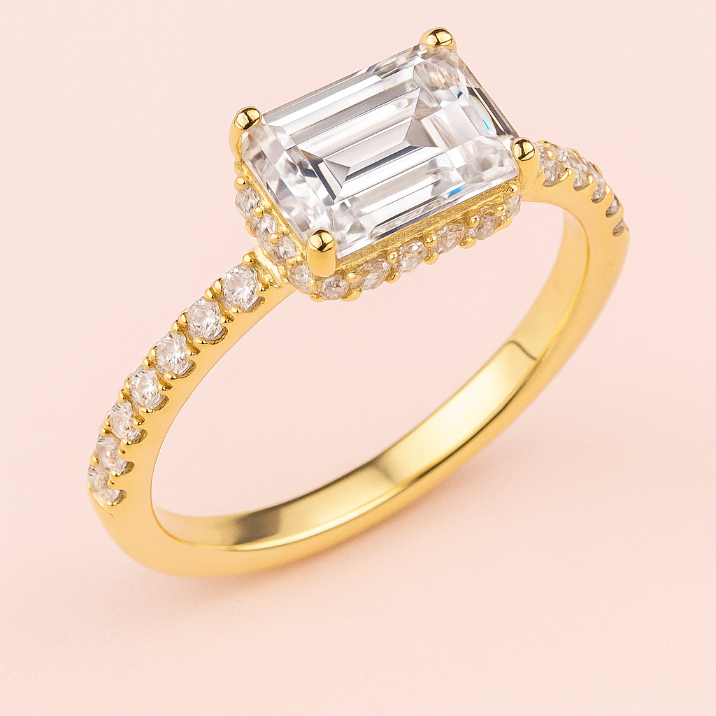 Gold ring with a large emerald-cut lab grown diamond and smaller diamonds on a pink background