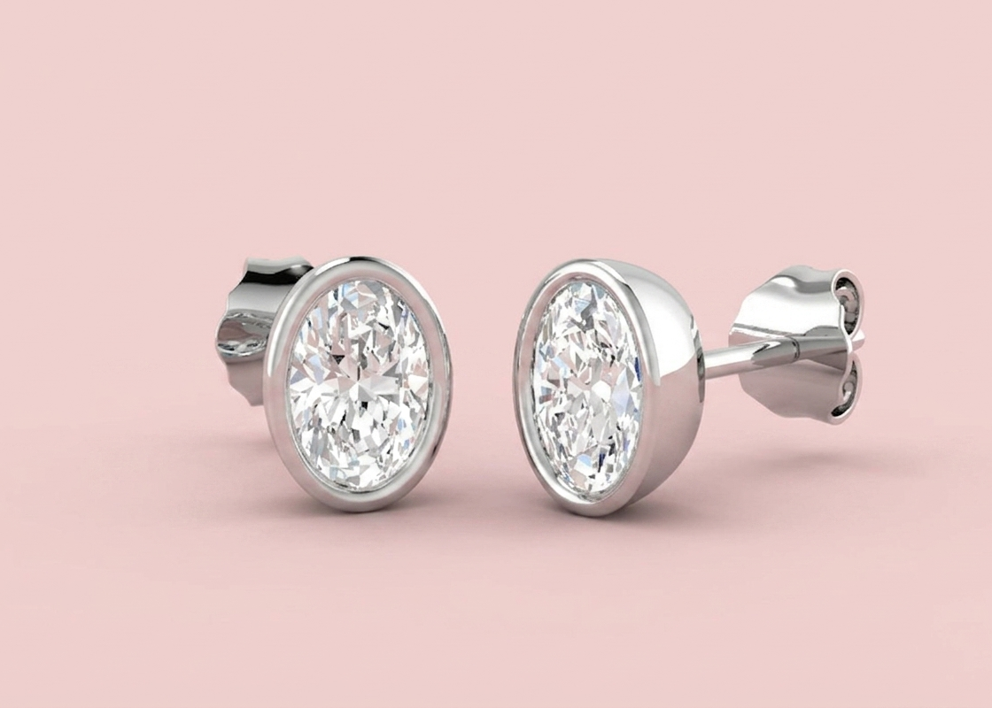 Bezel set lab grown oval diamond stud earrings shown in white gold on a pink background, in 1.12ct total