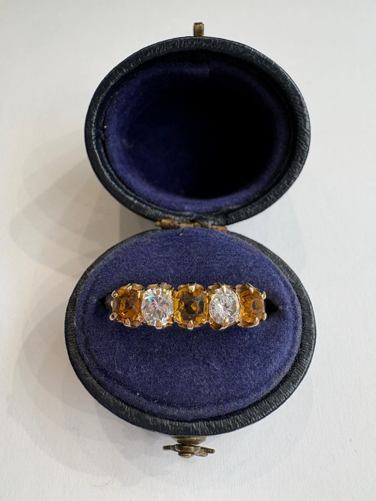A yellow gold ring with citrine and diamonds displayed inside an open round dark blue velvet jewelry box on a white background.