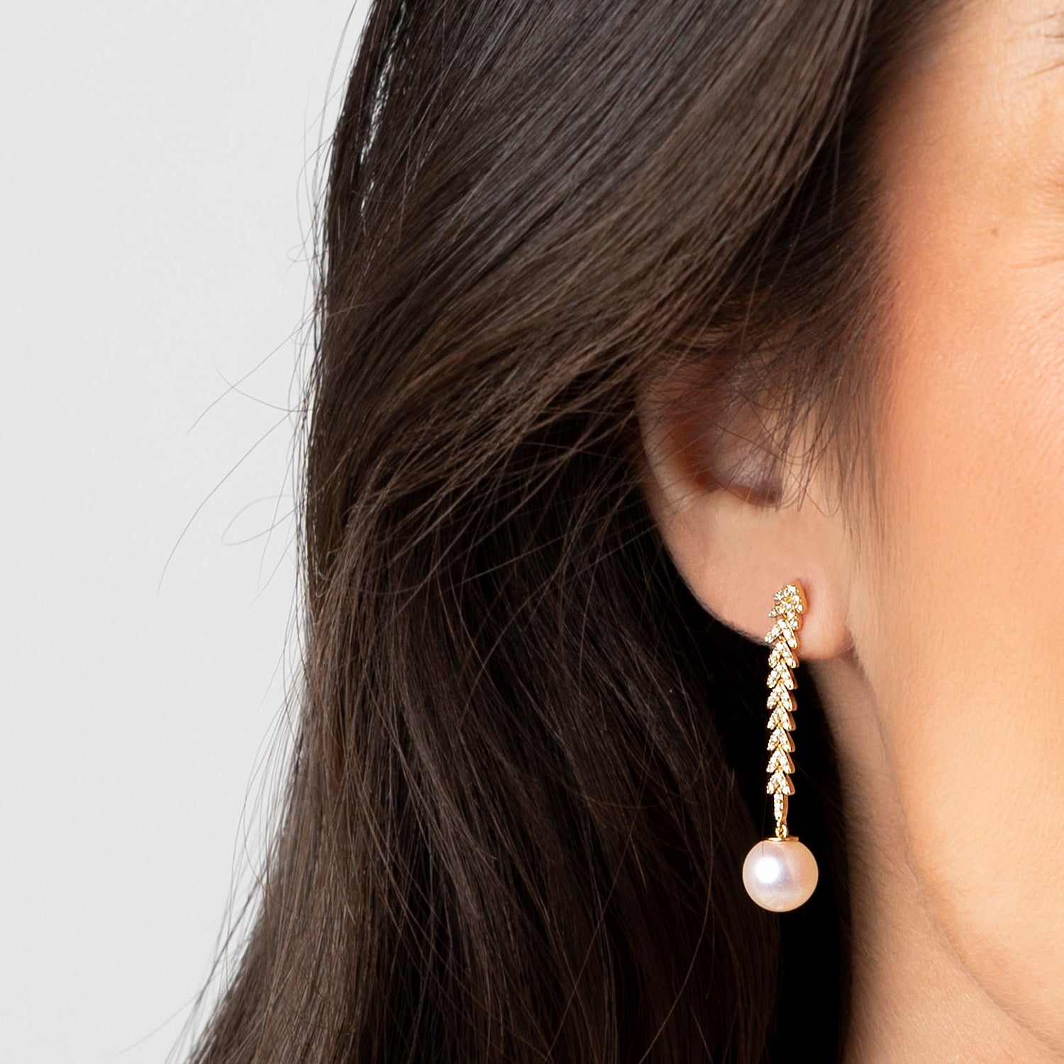 Yellow gold diamond chevron and Akoya pearl drop earrings featuring 106 round brilliant diamonds on a cascading spine with 8-8.5mm Akoya pearl drops, shown on model