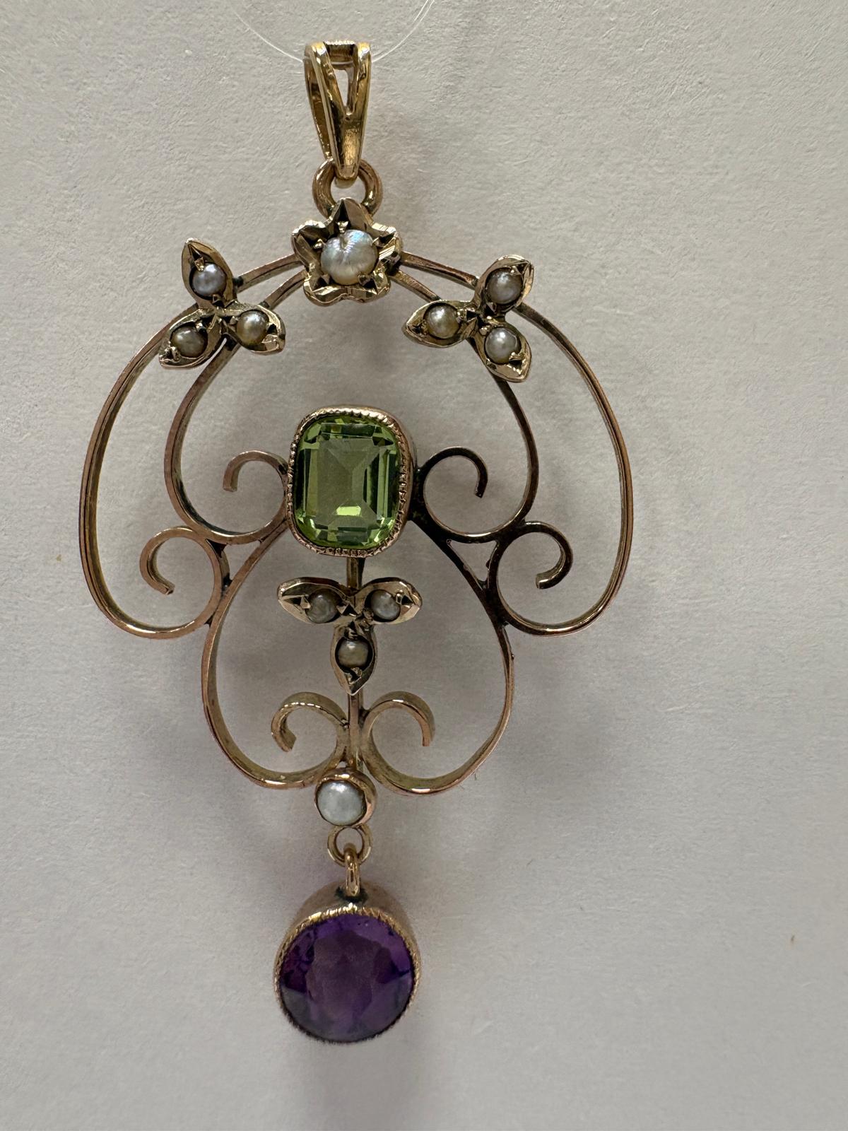 Gold pendant with green gemstone and purple stone on a white background