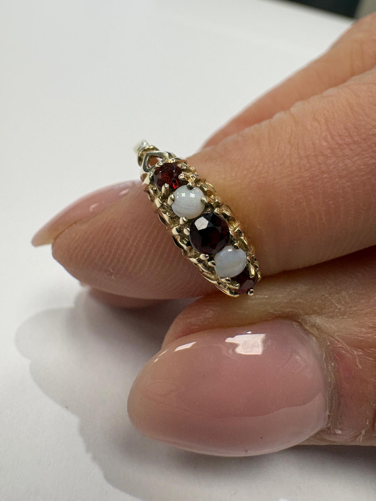 Gold ring with garnet and opal stones on a finger against a white background