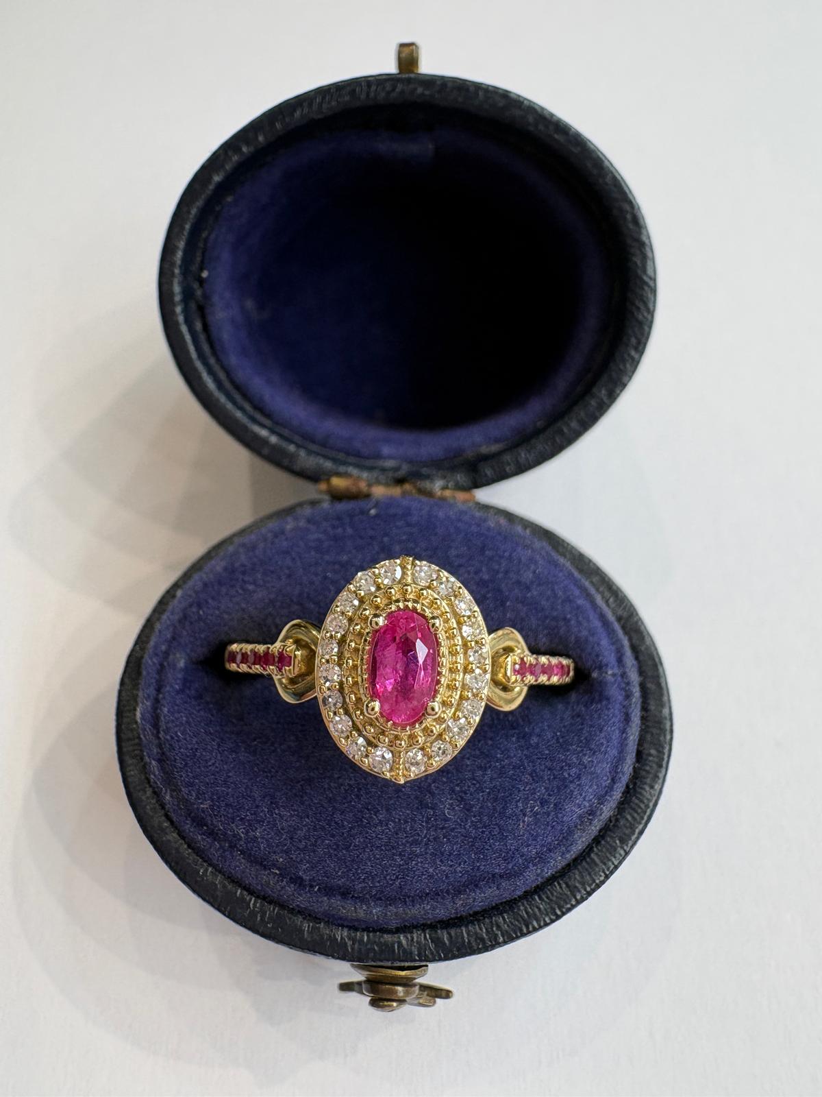 A vintage gold ring with a central oval ruby and surrounding diamonds, displayed inside an open dark blue velvet ring box on a white background.