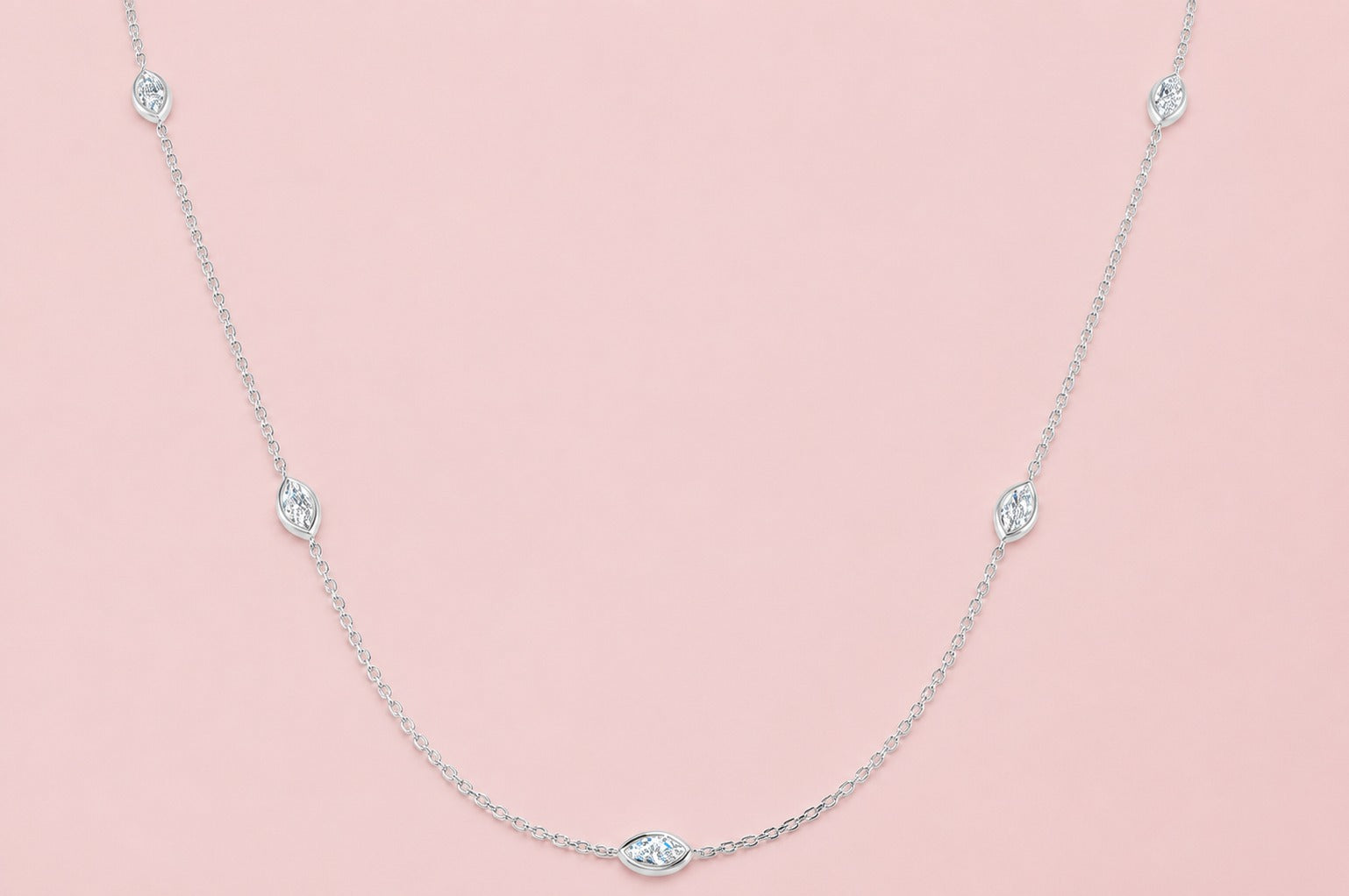 Bezel set lab grown marquise diamond station necklace on a delicate gold chain, shown in white gold versions on a pink background