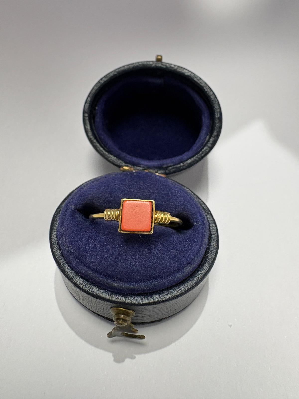 Pre-loved 14ct yellow gold natural coral dress ring presented in an antique navy blue velvet oval ring box. The square salmon-orange coral tablet is set in a yellow gold bezel with granulation detail on the shoulders, displayed against the deep blue velvet interior.