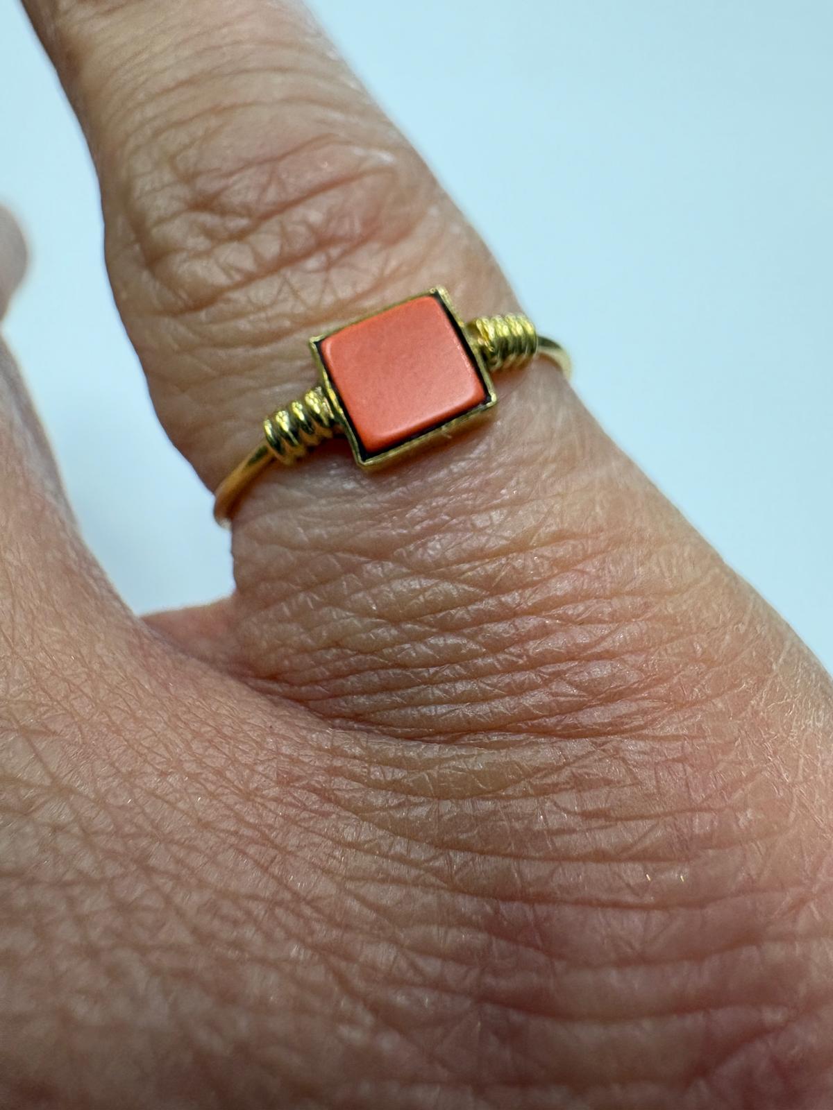 Close-up of a pre-loved 14ct yellow gold natural coral dress ring worn on a finger. The square salmon-orange natural coral tablet sits in a yellow gold bezel setting with fine granulation coil detail on both shoulders, shown on a slender gold shank.