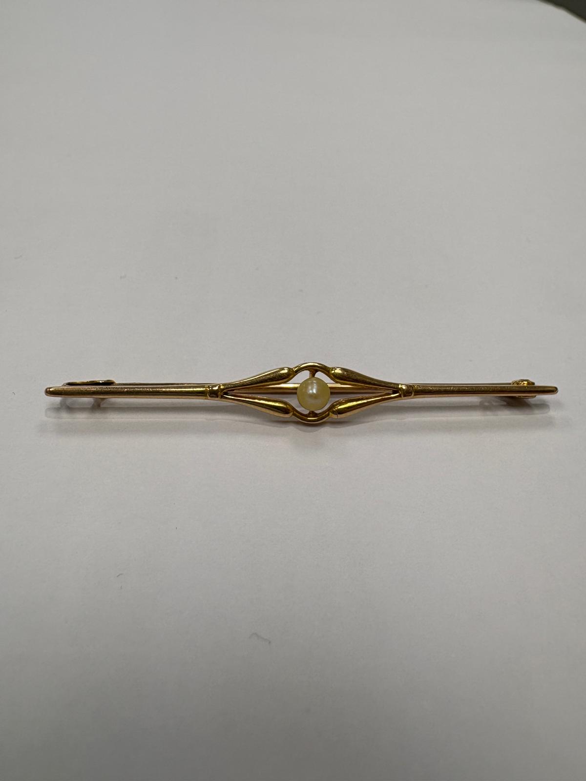 Front view of a pre-loved Edwardian 18ct yellow gold natural pearl bar brooch laid flat on a white surface. The slender tapering gold bar features an open scroll wing setting at the centre holding a single round natural pearl. Pin clasp visible to the right.
