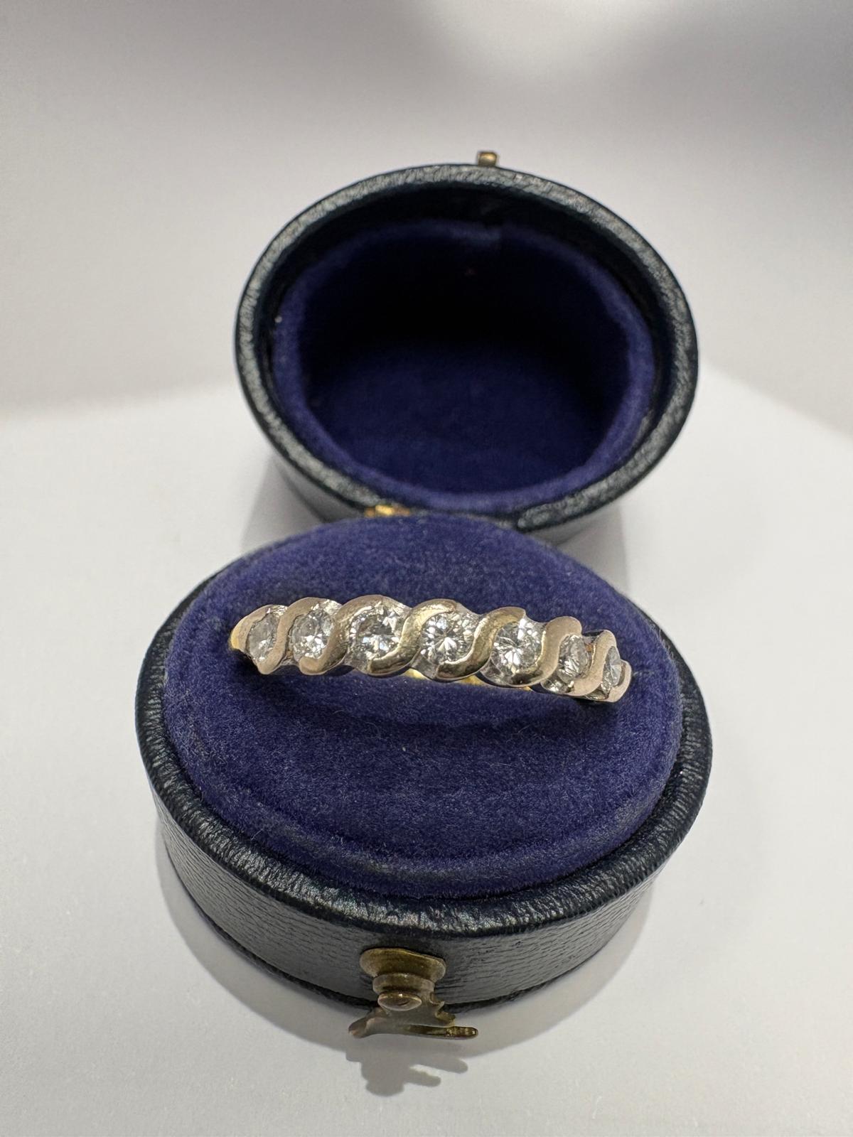 Front view of a pre-loved yellow gold diamond twist wave eternity ring displayed on an open antique navy blue velvet ring box cushion. The round brilliant cut diamonds are clearly visible seated within the continuous wave setting across the face of the ring.