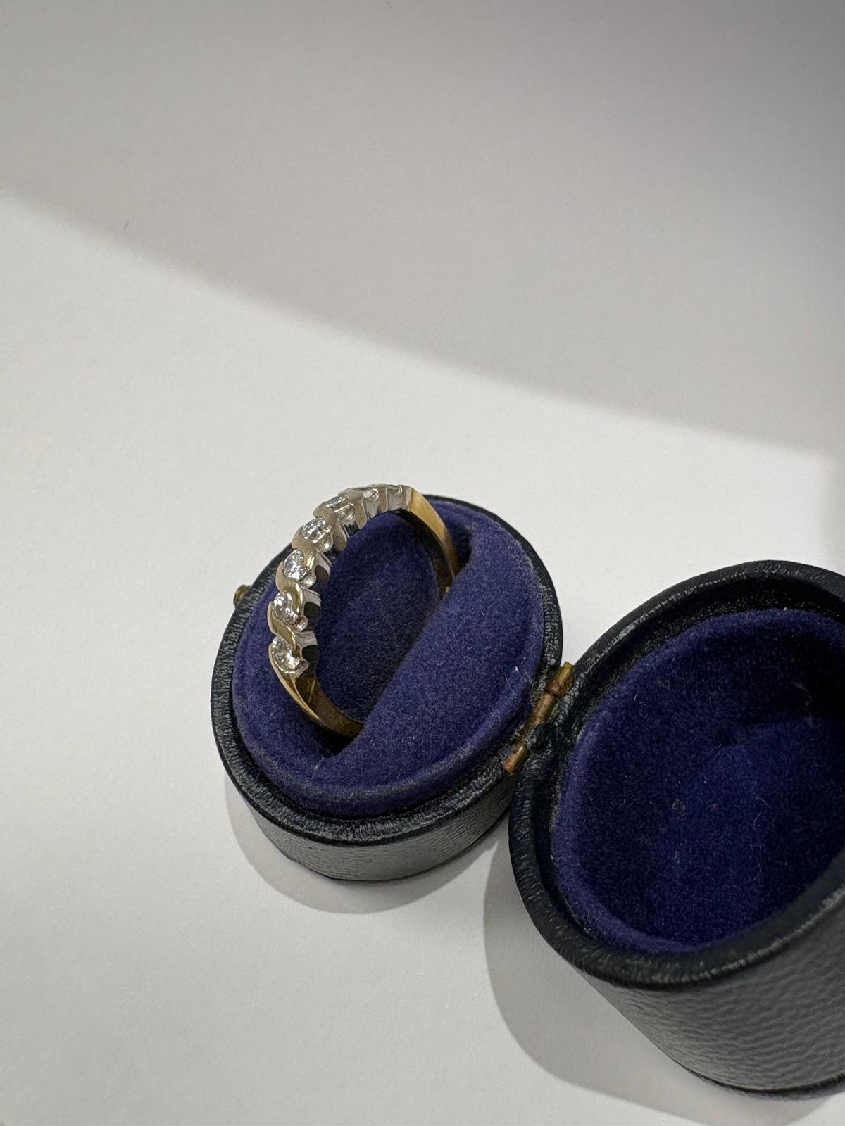 Side angled view of a pre-loved yellow gold diamond twist wave eternity ring balanced on the cushion of an open antique navy blue velvet oval ring box. The yellow gold shank and white gold twist diamond setting are clearly visible from this angle