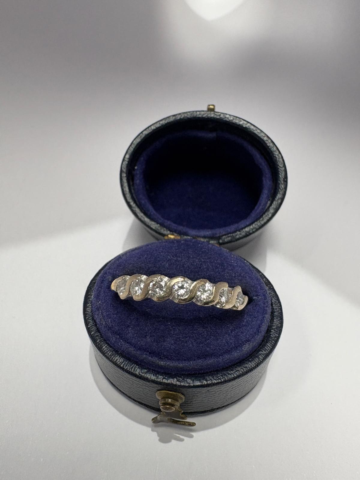 Top view of a pre-loved yellow gold diamond twist wave eternity ring resting on the cushion of an open antique navy blue velvet ring box. The ring features round brilliant cut diamonds set in a continuous wave or twist white gold setting across the face of the ring.