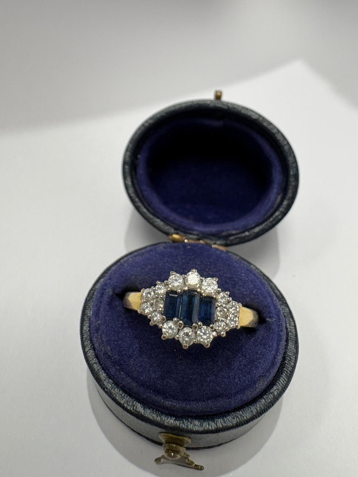 Angled view of a pre-loved yellow gold natural sapphire and diamond marquise cluster ring balanced on the cushion of an open antique navy blue velvet ring box. The yellow gold shank and the diamond and sapphire marquise cluster head are visible from this angle.