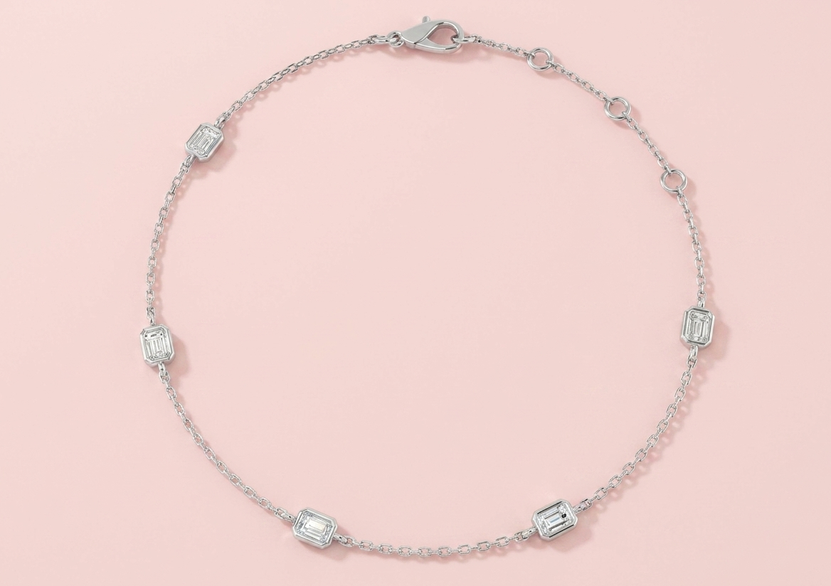 Bezel set lab grown emerald cut diamond station bracelet shown in white gold and yellow gold, featuring five emerald cut diamonds on a fine chain with lobster clasp and extender