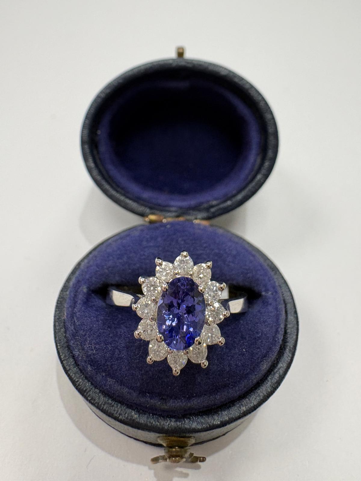 An oval tanzanite ring with a halo of small diamonds, displayed inside an open dark blue velvet ring box