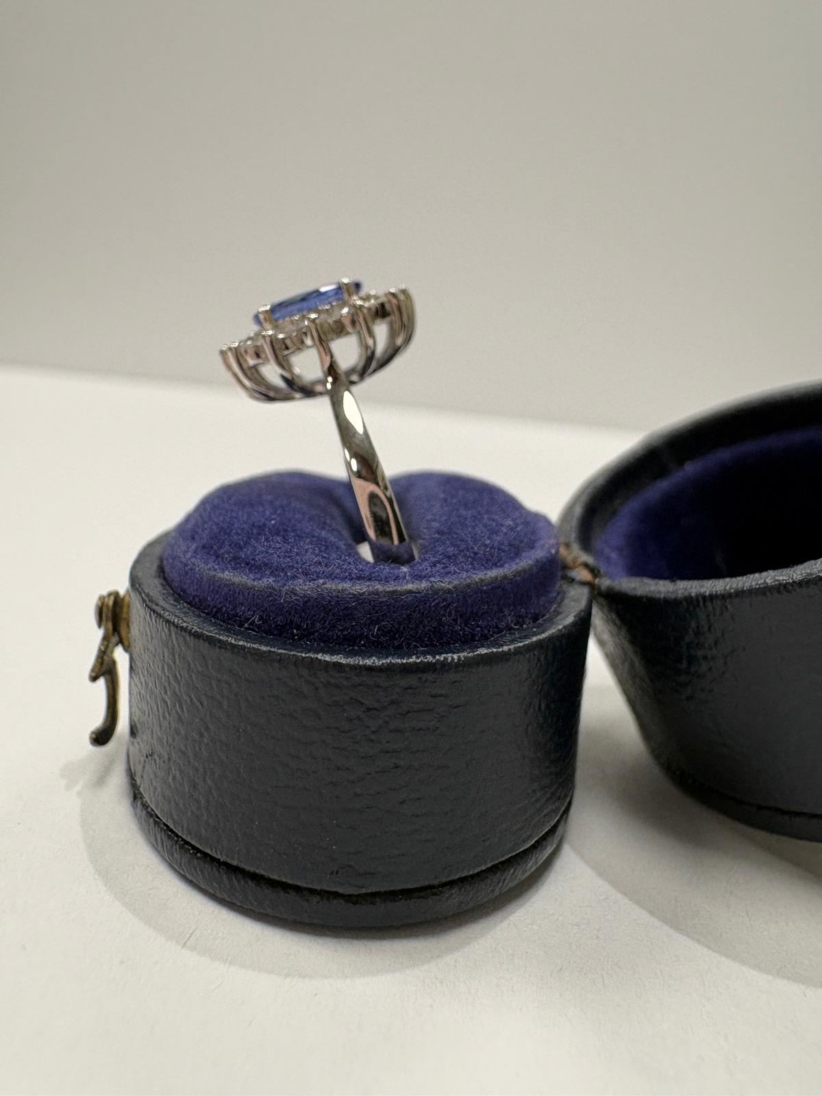An oval tanzanite ring with a halo of small diamonds, displayed inside an open dark blue velvet ring box