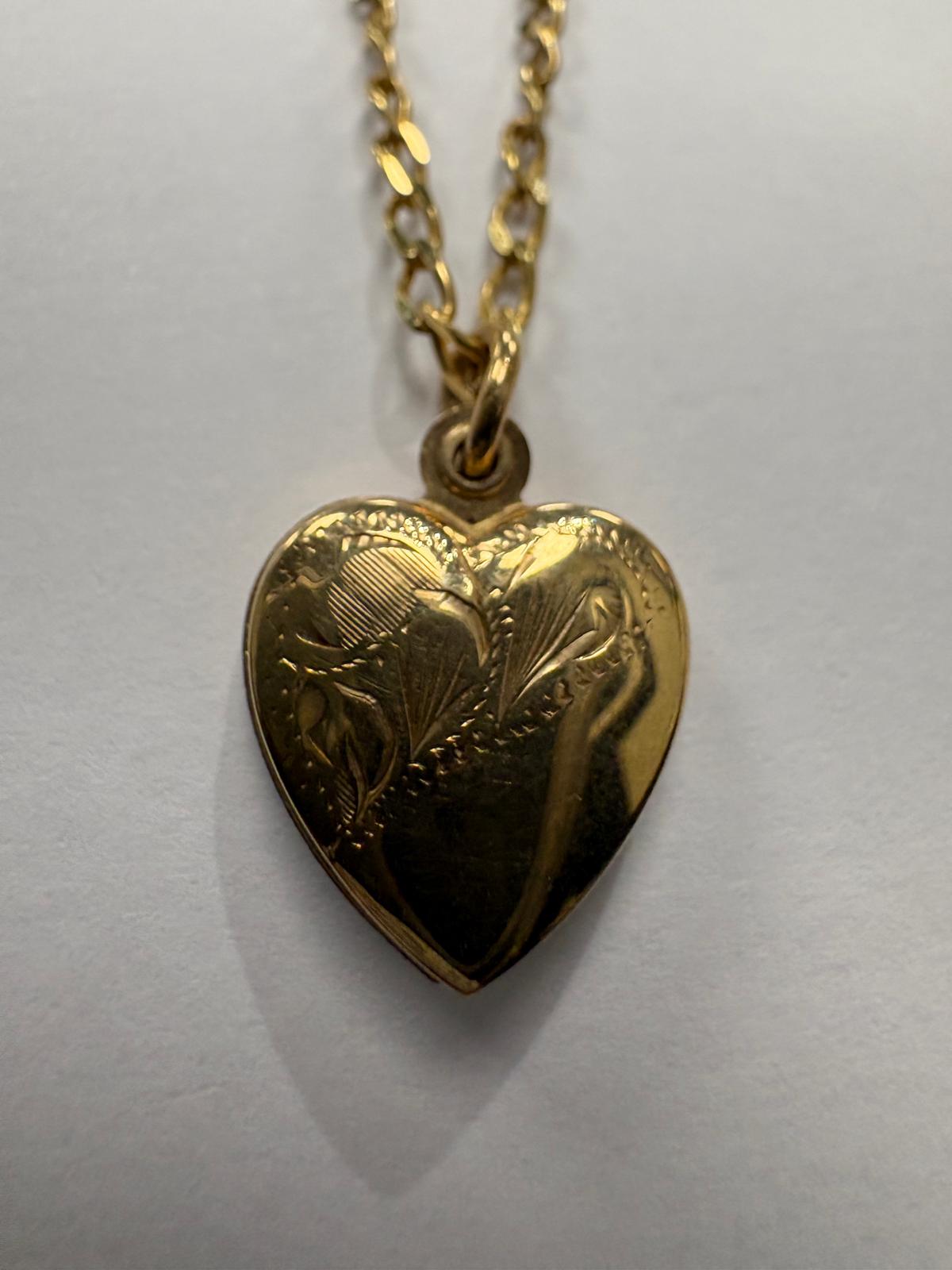 Close-up front view of a vintage 9ct yellow gold domed heart locket showing detailed hand-engraved foliate and floral decoration. The engraving features feather-like leaves and botanical motifs across the surface, with a beaded border around the edge of the heart.