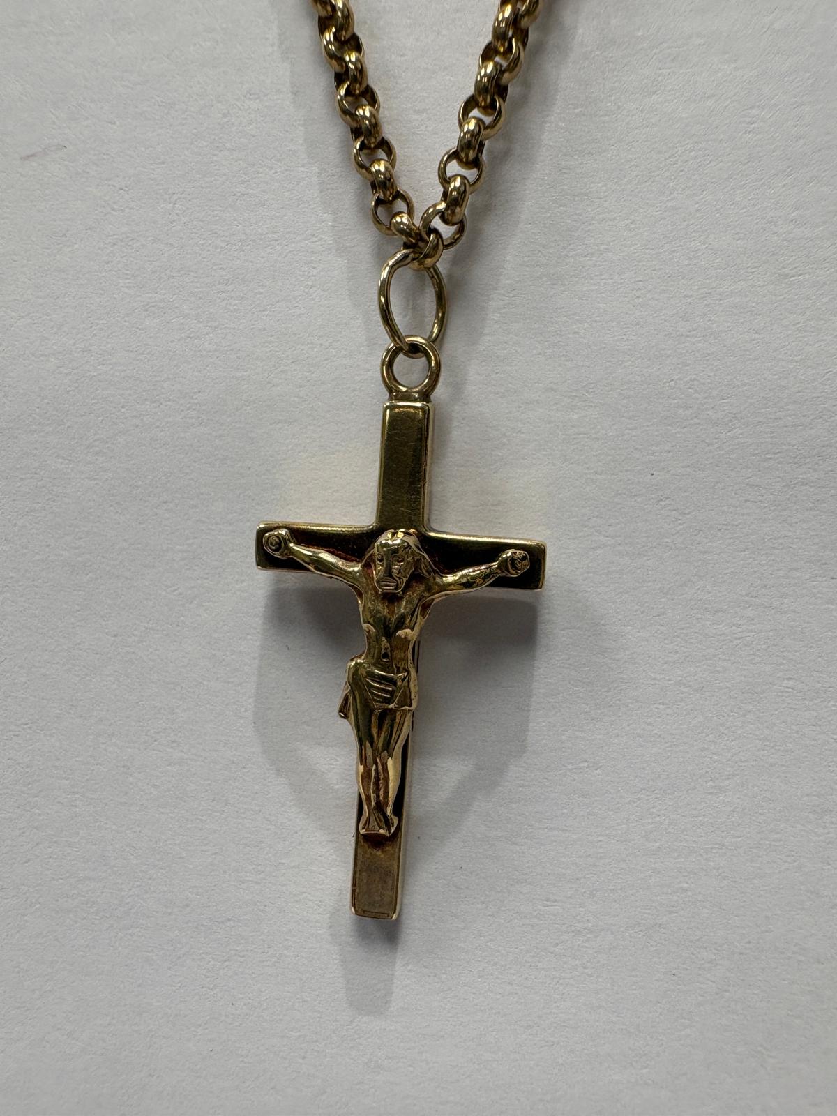 Full length view of a yellow gold necklace laid flat on a grey background. A yellow gold belcher link chain suspends a plain polished yellow gold crucifix pendant with a detailed corpus of Christ figure.