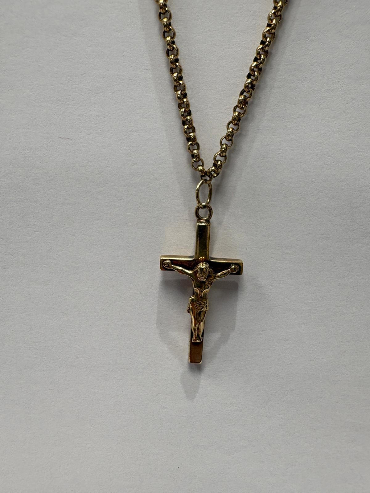 Three-quarter length view of a yellow gold crucifix pendant necklace laid flat on a grey background. The plain polished yellow gold cross features a detailed corpus of Christ figure. It hangs from a chunky yellow gold belcher link chain.