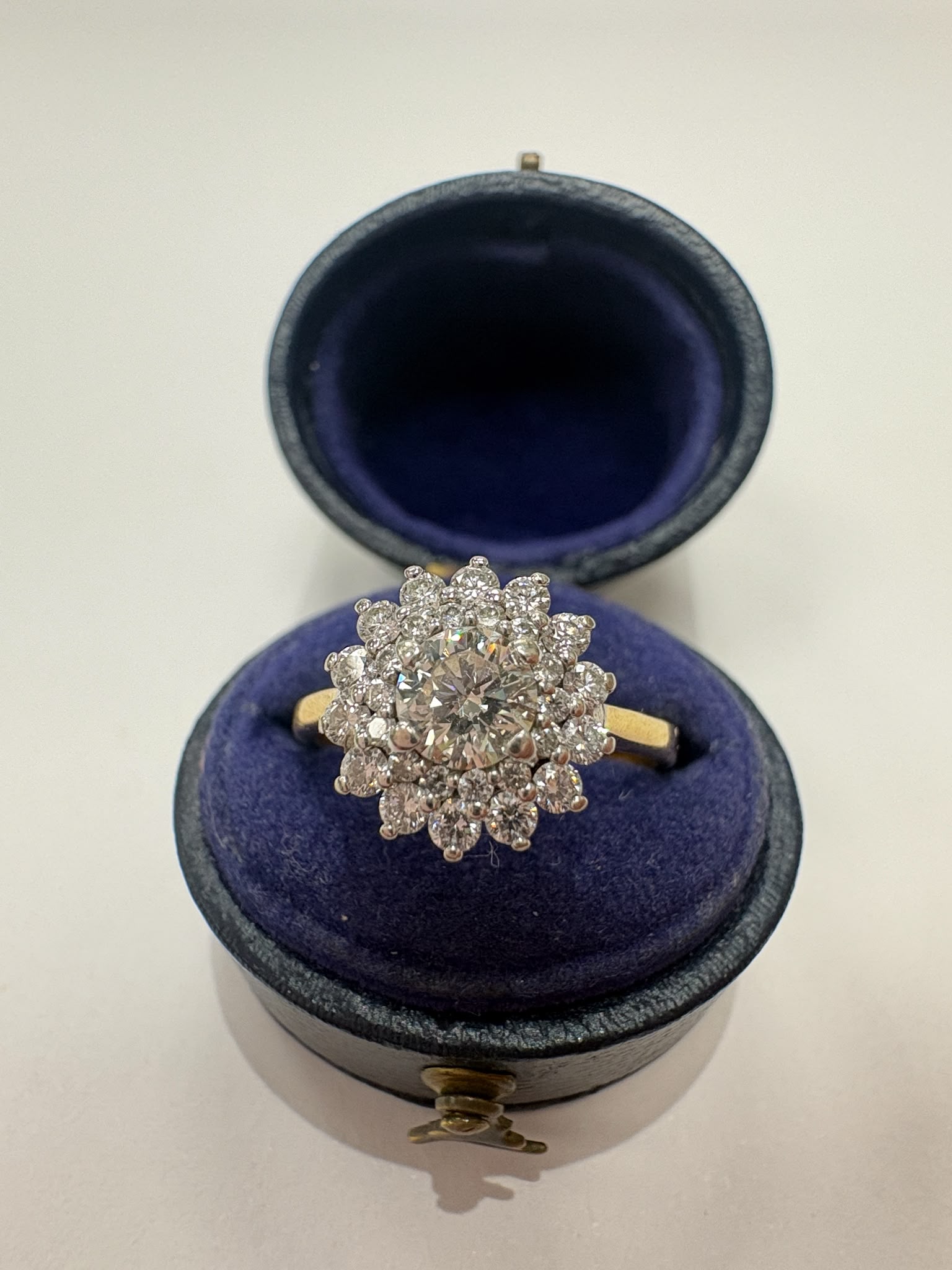 A yellow gold ring with a large diamond cluster setting, displayed inside an open dark blue velvet ring box on a light background.