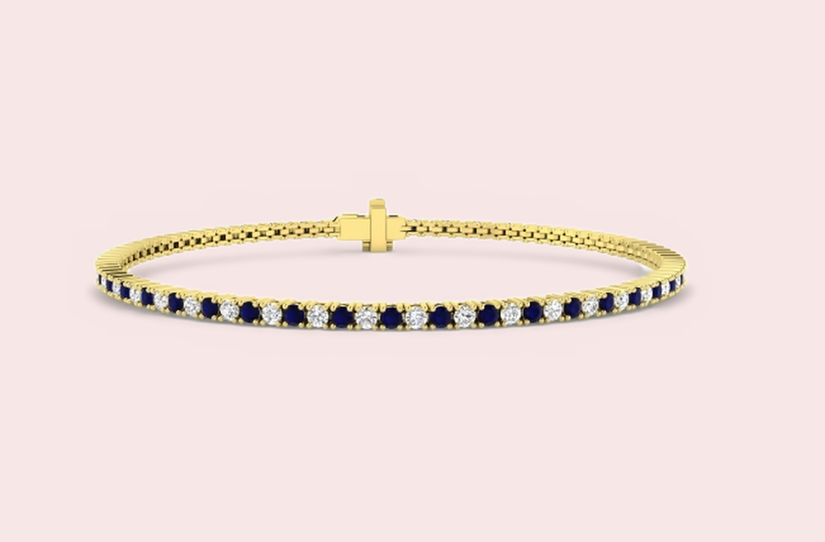Yellow gold tennis bracelet set with alternating lab-grown blue sapphires and diamonds, on a pale pink background