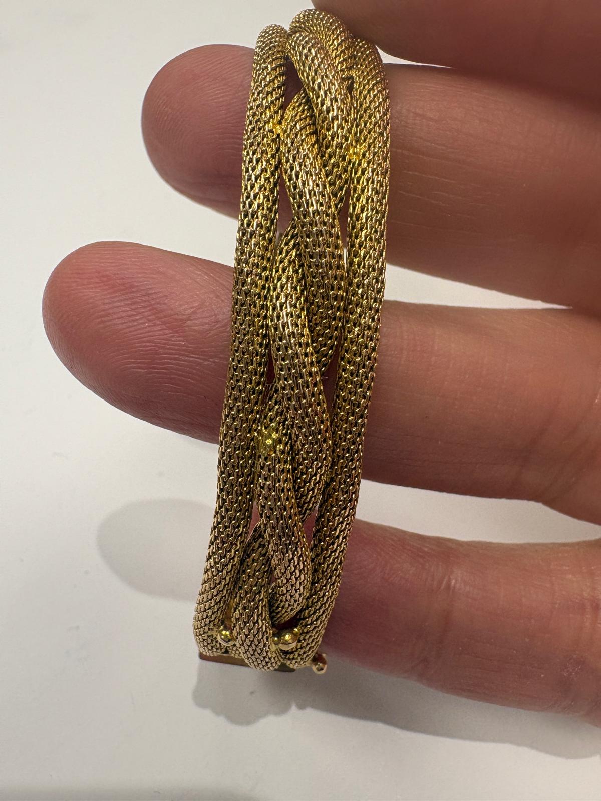 Gold chain bracelet held between fingers on a white background