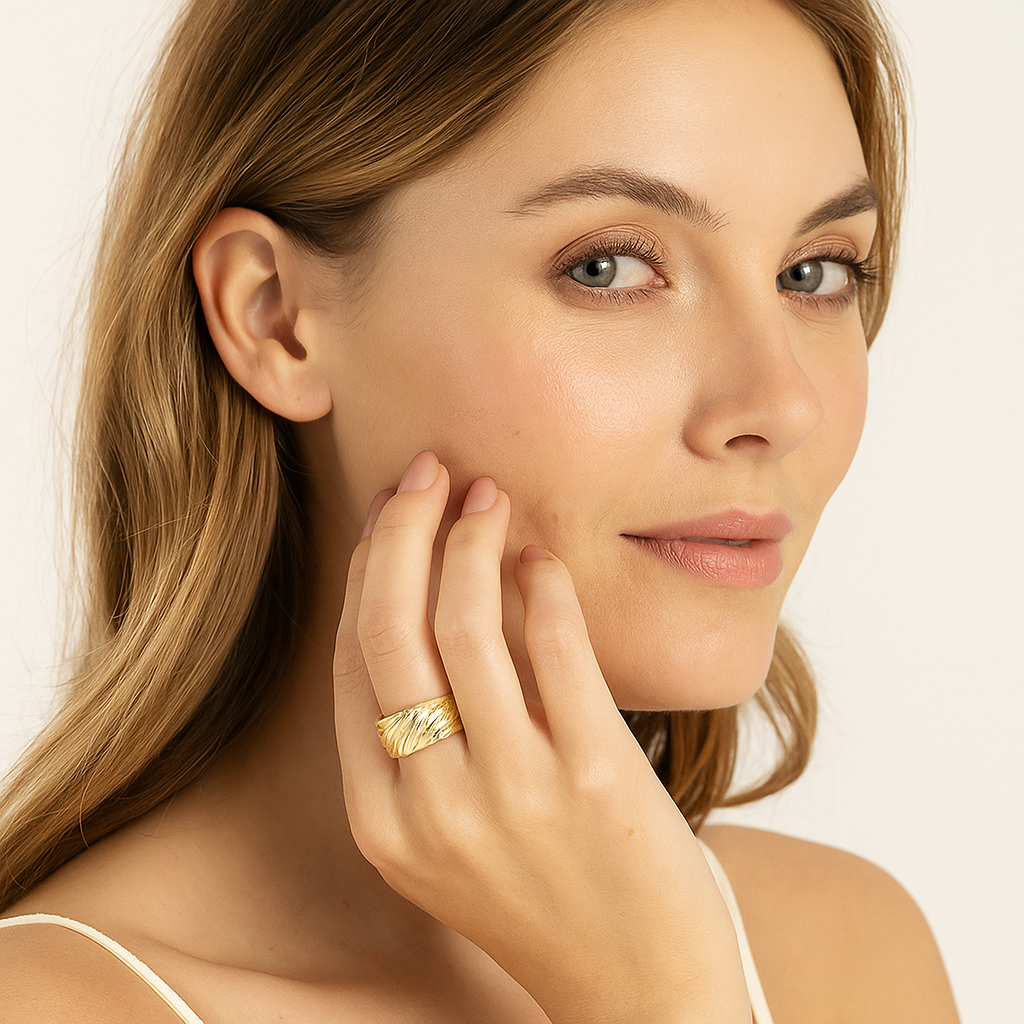Woman wearing a gold ring on her finger, touching her face against a neutral background