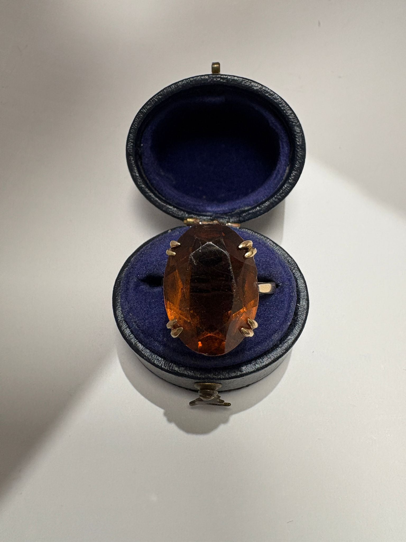 Ring with a large orange gemstone in an open jewelry box on a white background