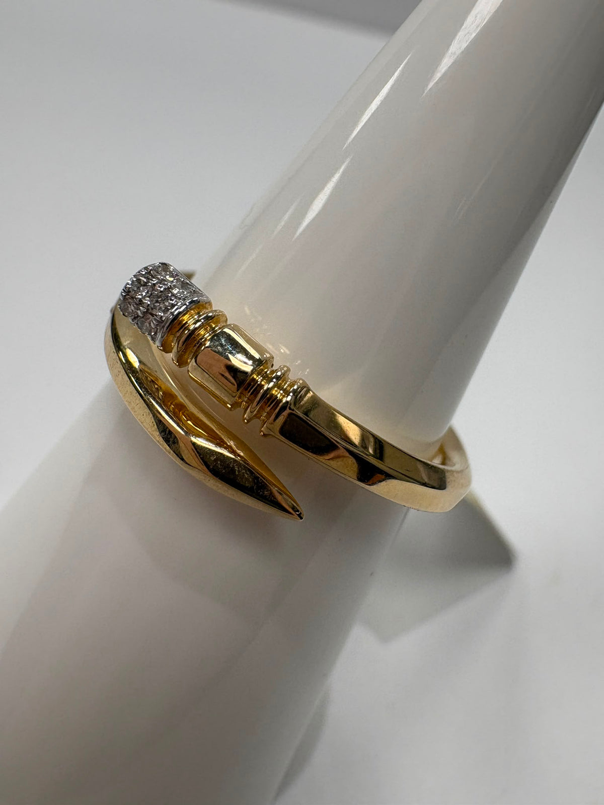 A gold ring with a textured pavé-set clear stone cluster on one end and a polished pointed claw-like accent on the other, displayed on a white cone stand.
