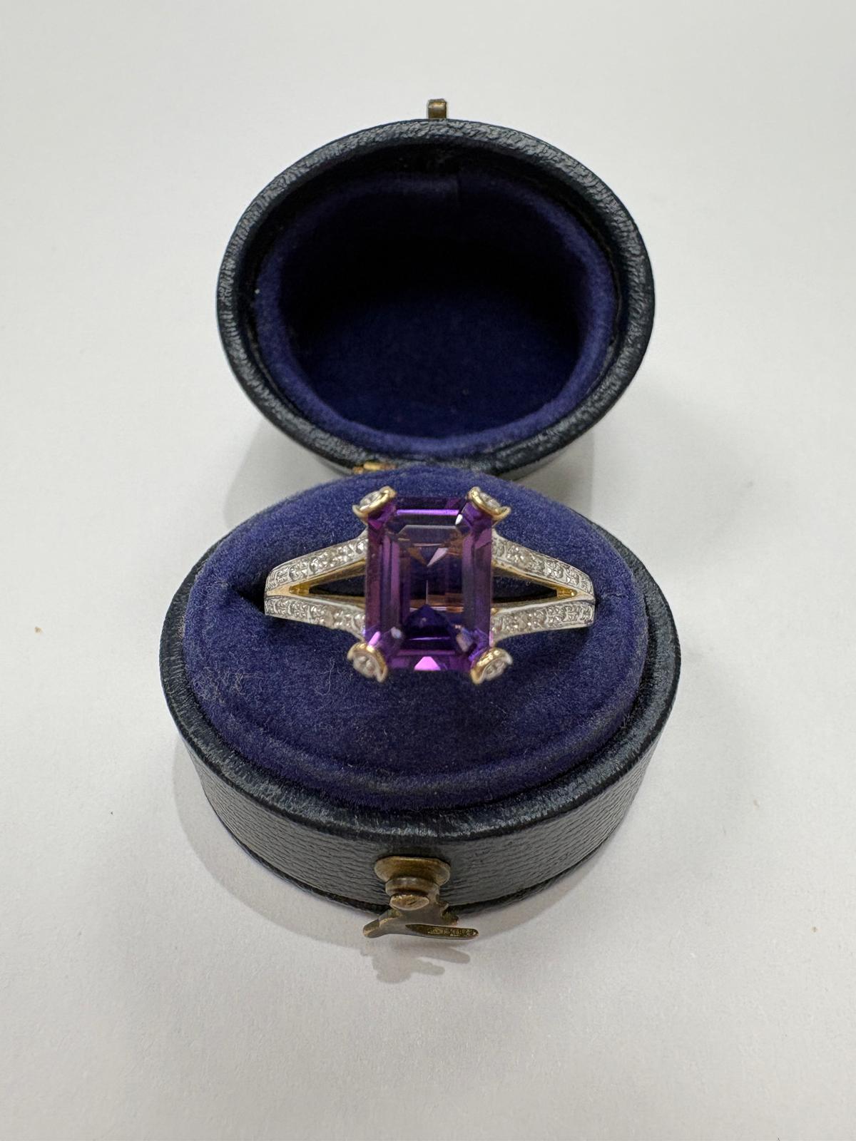 A ring with an amethyst on split shoulders, displayed inside an open round blue ring box 
