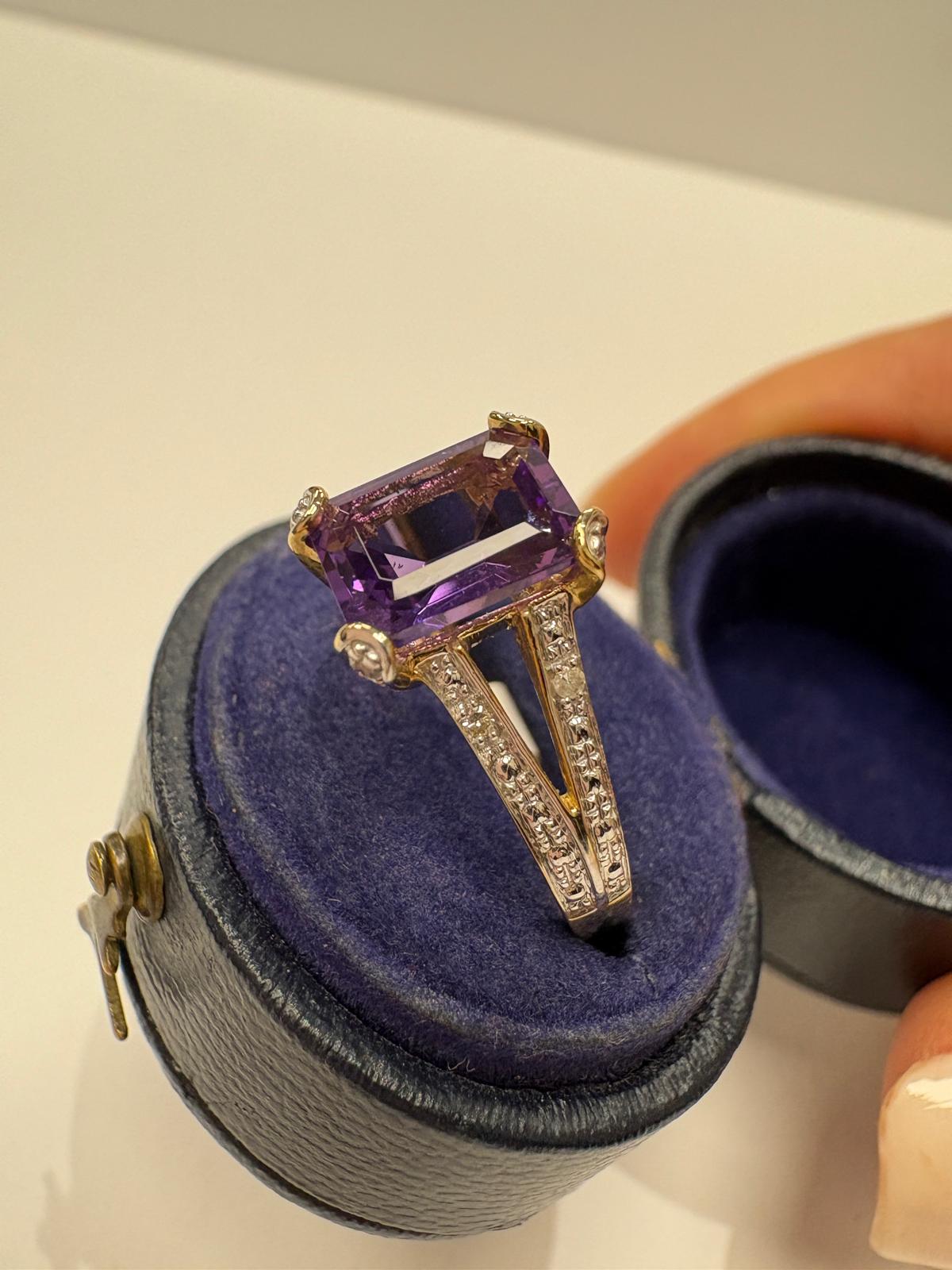 A ring with an amethyst on split shoulders, displayed inside an open round blue ring box 