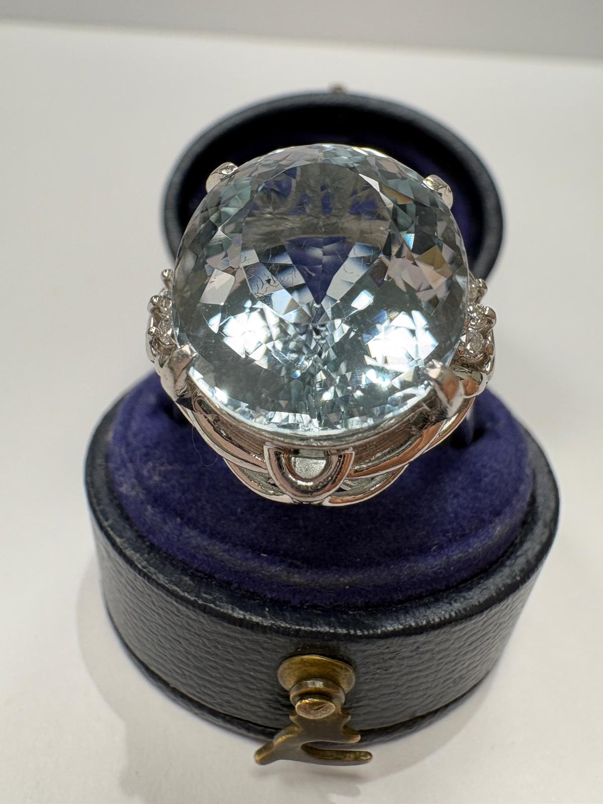 A large oval-cut aquamarine ring in a silver-toned setting, displayed on top of a vintage ring box 