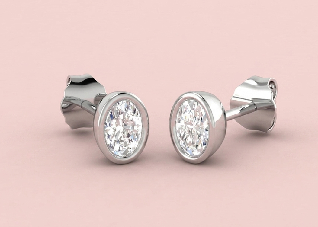 Bezel set lab grown oval diamond stud earrings shown in white gold on a pink background, 0.52ct 