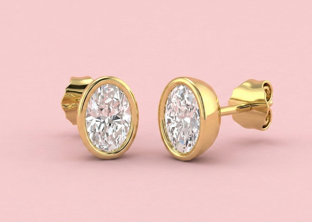  Bezel set lab grown oval diamond stud earrings shown in yellow gold on a pink background, in 1.12ct 