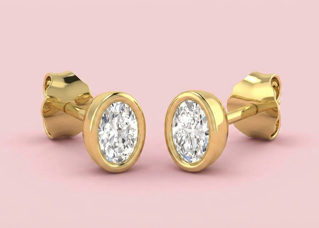 Bezel set lab grown oval diamond stud earrings shown in yellow gold on a pink background, in 0.52ct 