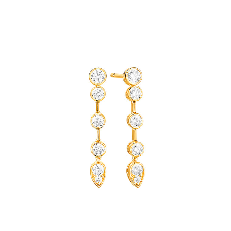 Yellow gold bezel set diamond drop earrings featuring a descending line of round brilliant diamonds finished with a pear shaped diamond, shown on white background