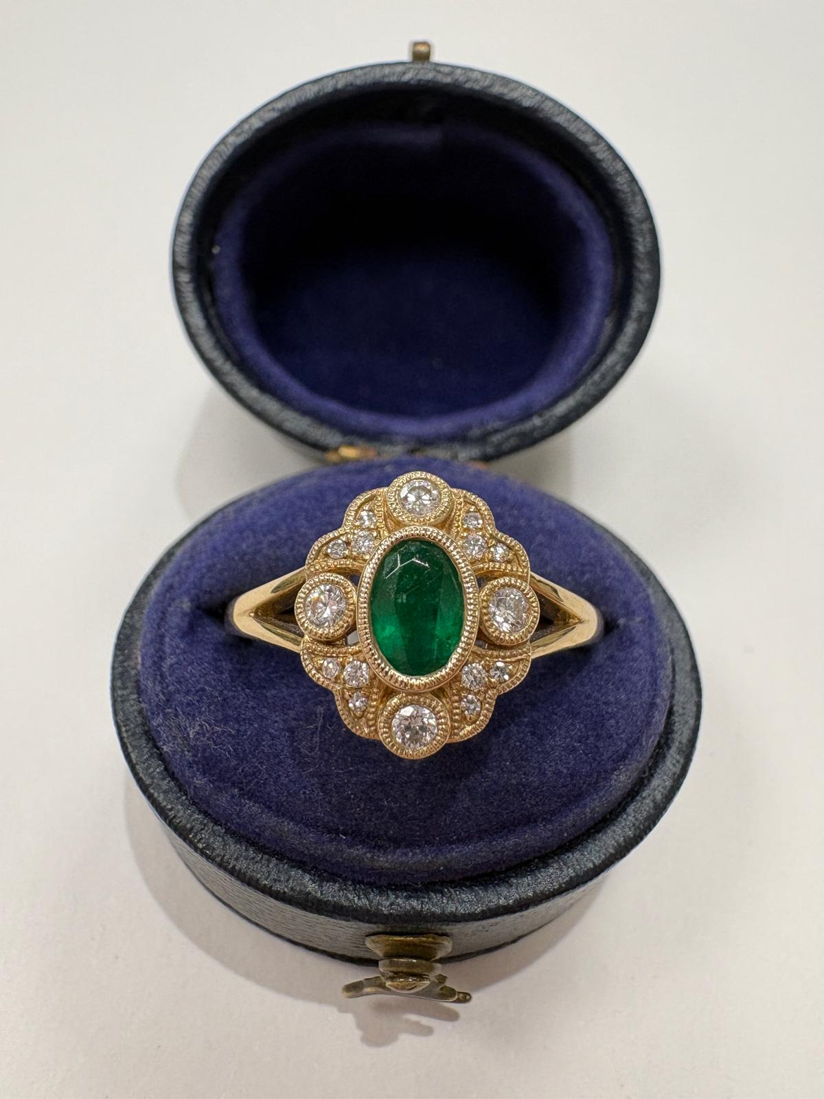 A vintage-style gold ring with a central oval green emerald and surrounding diamonds, set with a milgrain edge