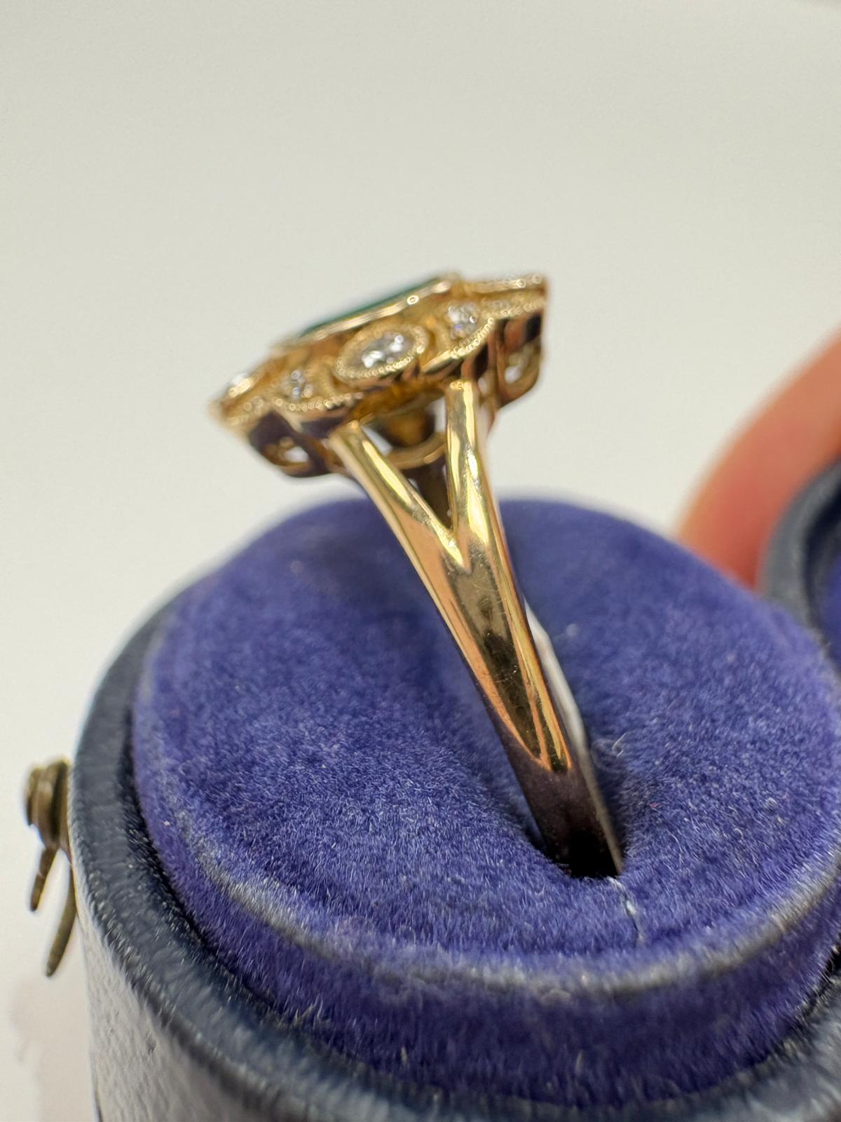 A vintage-style gold ring with a central oval green emerald and surrounding diamonds, set with a milgrain edge