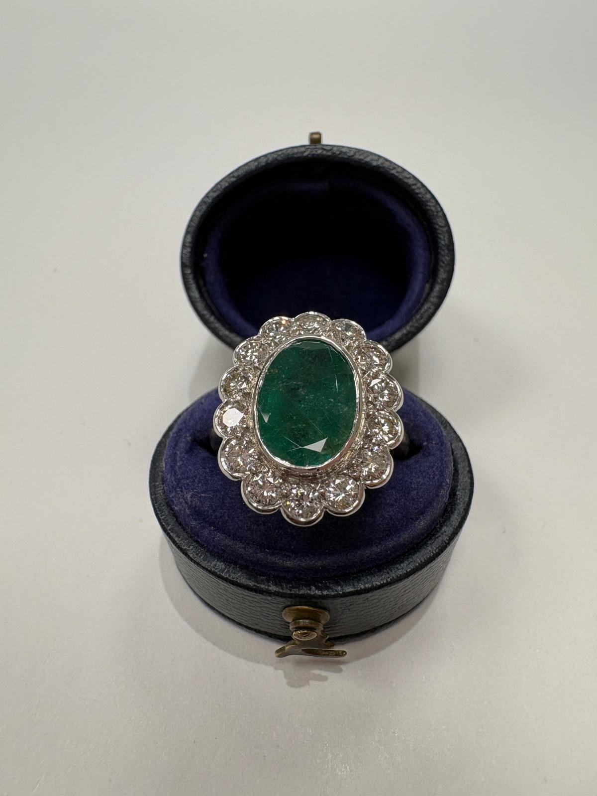 An oval emerald and diamond ring with a scalloped halo, displayed inside an open dark blue velvet ring box 