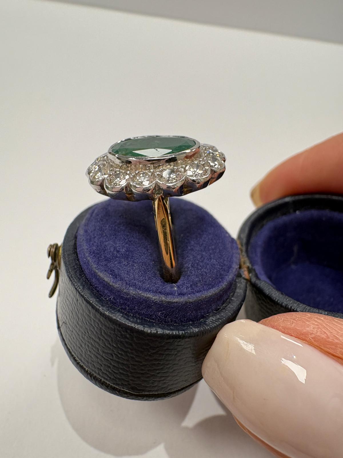 An oval emerald and diamond ring with a scalloped halo, displayed inside an open dark blue velvet ring box 