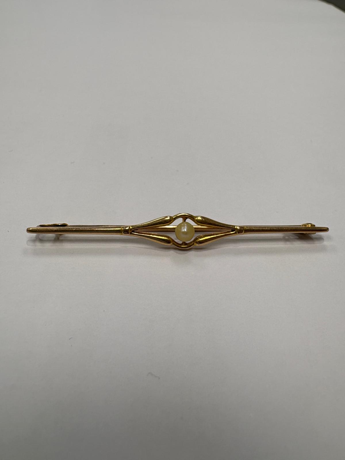 Side view of a pre-loved Edwardian 18ct yellow gold natural pearl bar brooch with the pin mechanism open. The slender gold pin is shown extended from the catch, demonstrating the full length and depth of the brooch. The open scroll pearl centrepiece is visible from the side.
