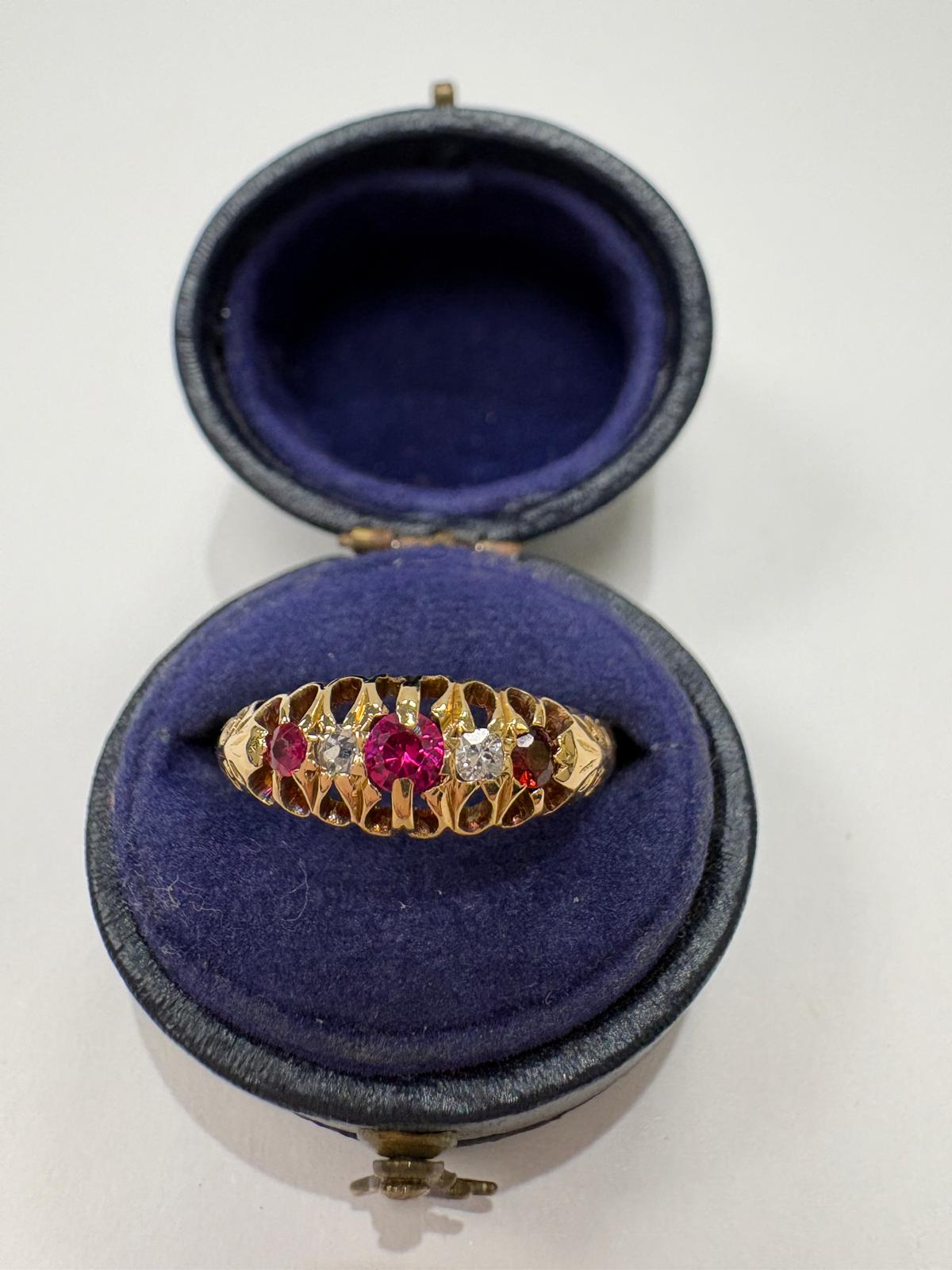 A vintage yellow gold ring with a central ruby and side diamonds, displayed inside an open round velvet jewelry box 