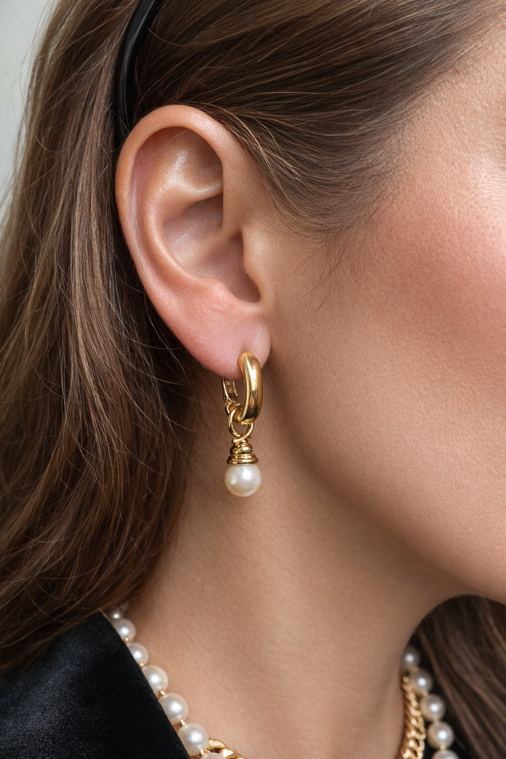 Close-up of a gold hoop earring with a pearl drop worn by a Mona Norman.