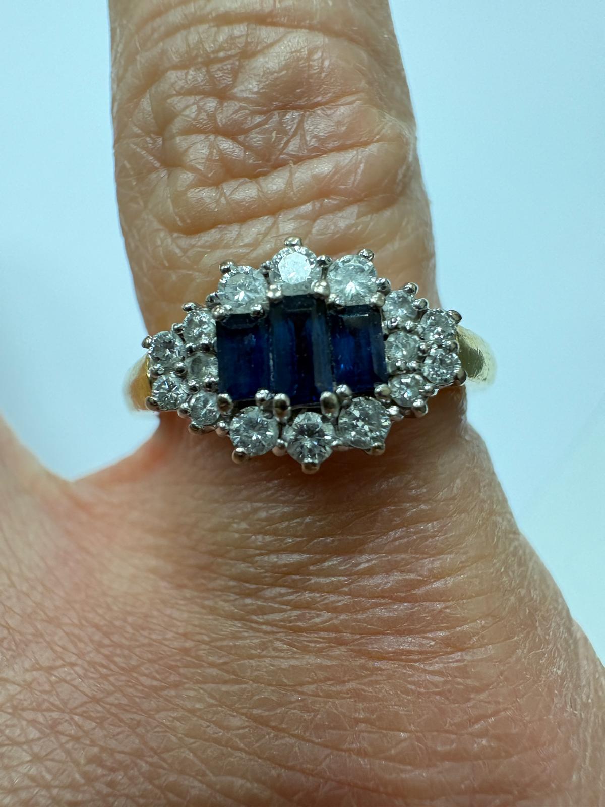 Angled view of a pre-loved yellow gold natural sapphire and diamond marquise cluster ring balanced on the cushion of an open antique navy blue velvet ring box. The yellow gold shank and the diamond and sapphire marquise cluster head are visible from this angle.