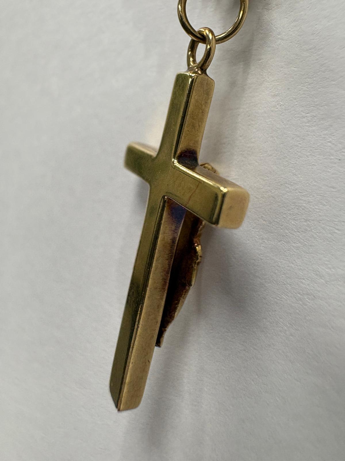Close-up view of the reverse side of a yellow gold crucifix pendant. The plain polished back of the cross with bevelled edges is shown. The jump ring is visible at the top.
