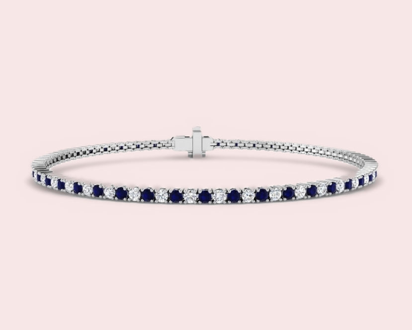 White gold tennis bracelet set with alternating lab-grown blue sapphires and diamonds, on a pale pink background