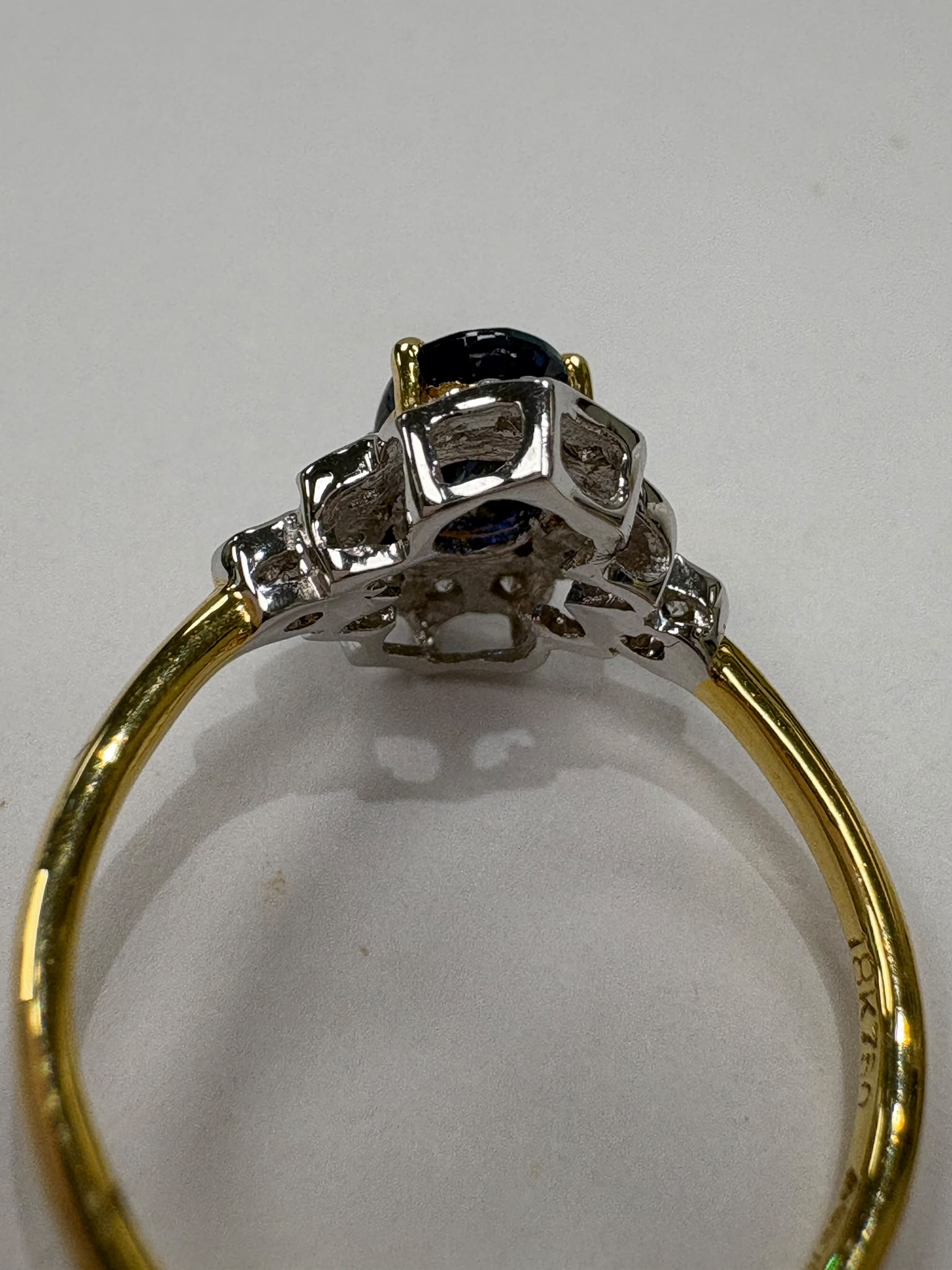 A close-up shot of a vintage-style ring featuring a yellow gold band, a silver-toned geometric setting, and a dark blue oval gemstone in the center.