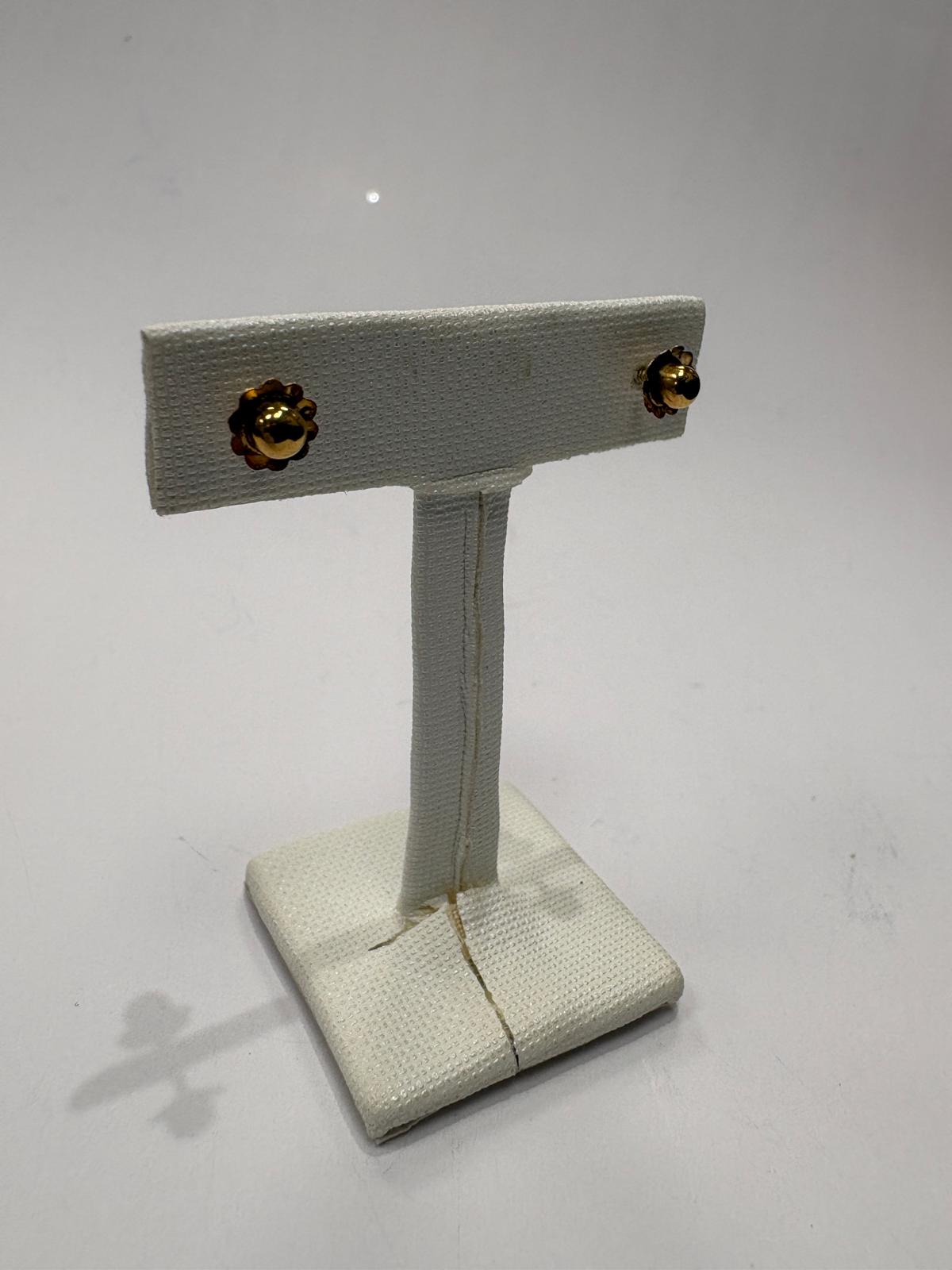 Gold stud earrings on a beige earring stand against a white background