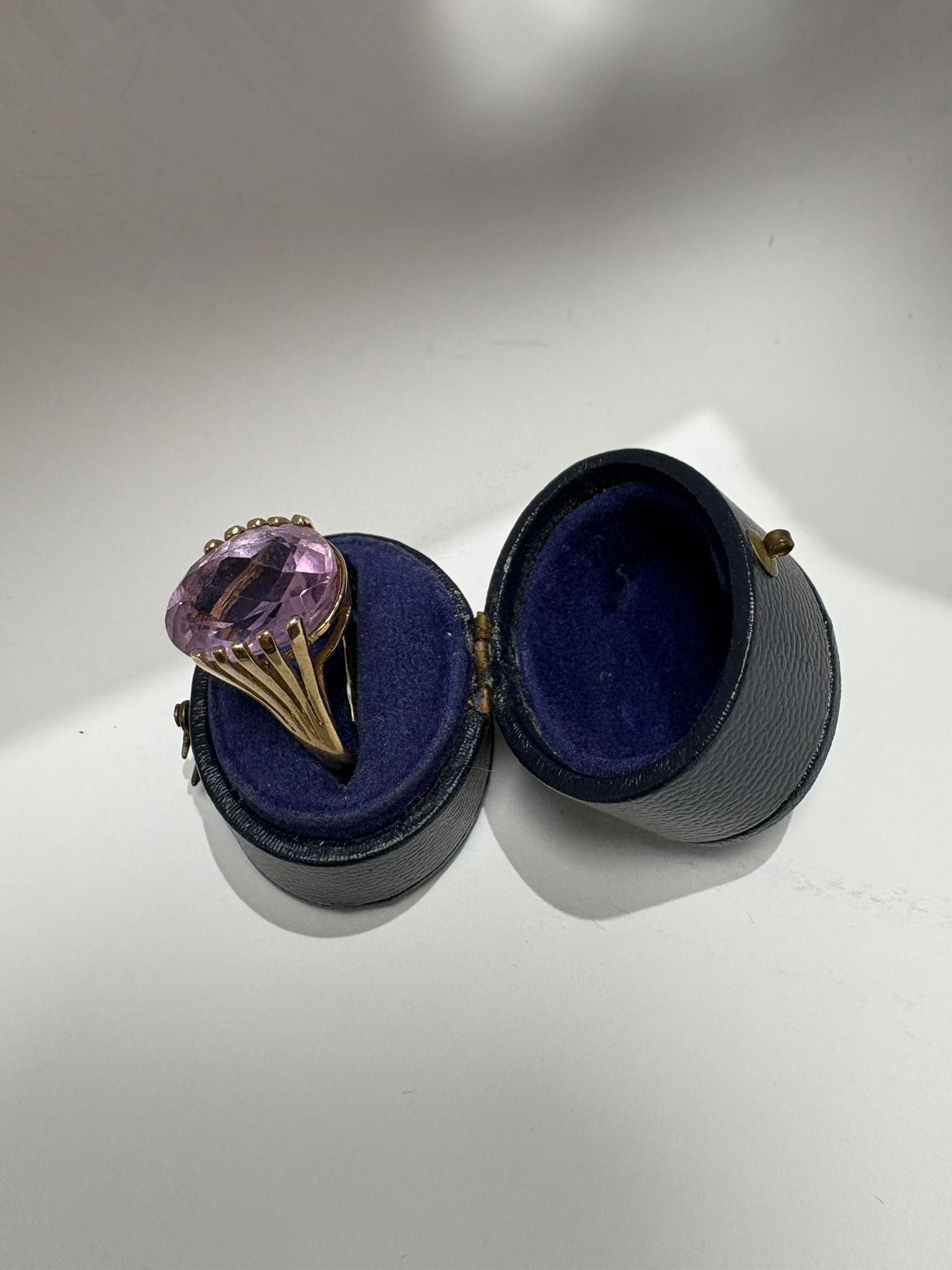 Ring with a purple gemstone in an open jewelry box on a white surface
